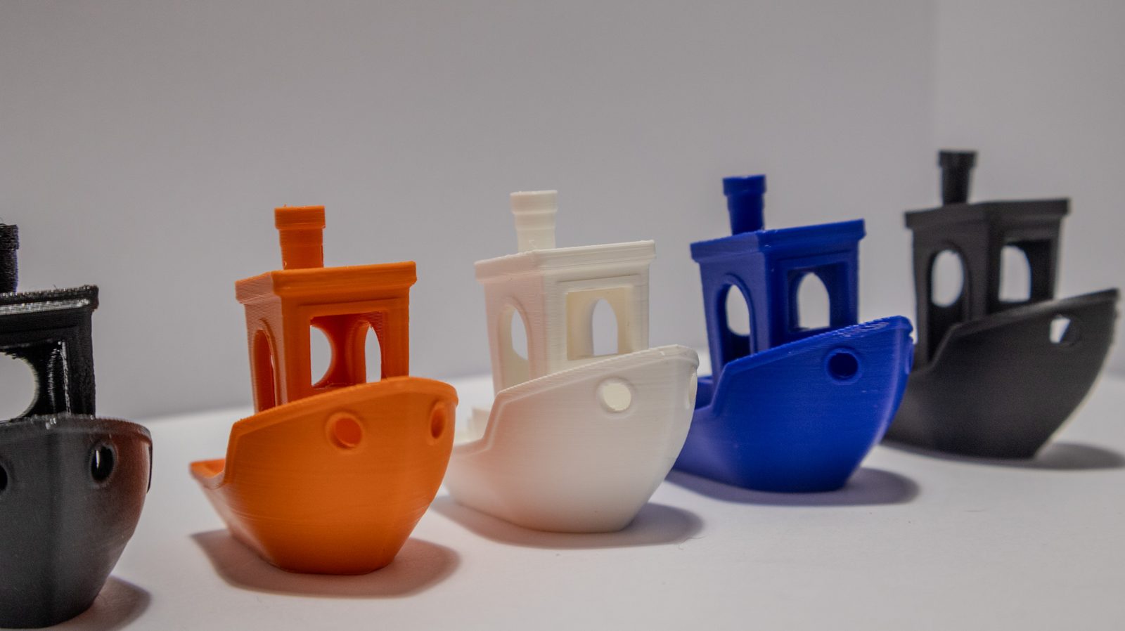 Fünf gleiche Schiffsmodelle in diagonaler Reihe gestaffelt, in Anthrazit, Orange, Weiß, Blau und Schwarz